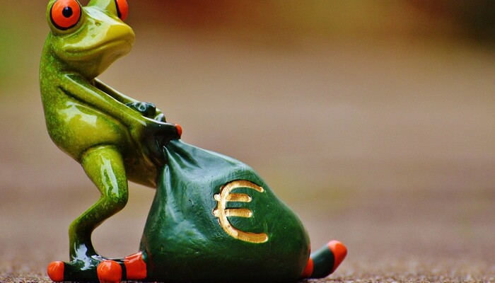Kuvassa on posliininen vihreä sammakko, joka raahaa tumman vihreää rahasäkkiä.